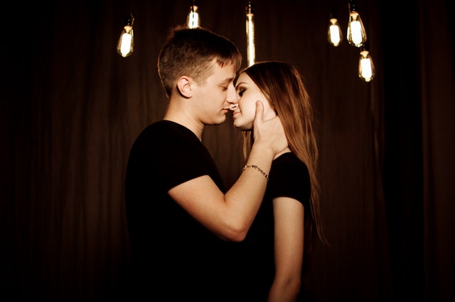 Chlap drží ženu za tvár v miestnosti s žiarovkami na strope.jpg